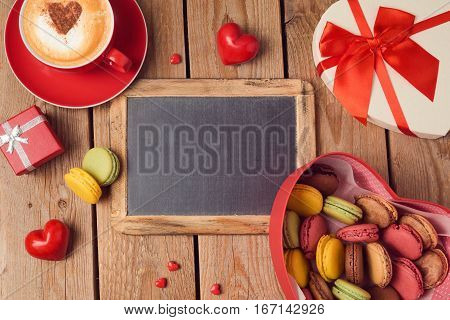 Valentines day concept with macarons coffee cup and chalkboard over wooden background. Top view from above