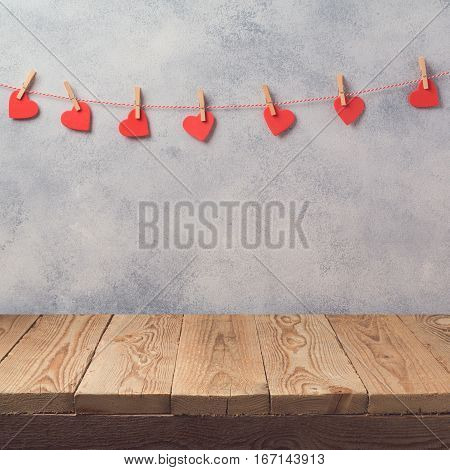 Empty wooden deck table over rustic wall background with heart shape garland. Valentines day concept