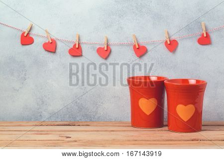 Valentines day concept with coffee cups and heart shapes over rustic background with garland