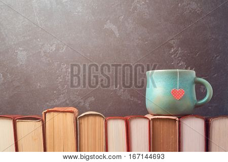 Valentines day concept with tea cup on books over blackboard background