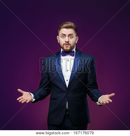 Handsome man in tuxedo and bow tie is surprised and throws his hands. compere in fashionable, festive clothing on dark background