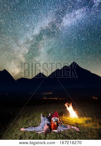 Young Couple Tourists Lying Near The Campfire Under Incredibly Beautiful Starry Sky And Milky Way At
