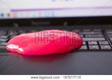 Keyboard cleaning gel is laying on the notebook. Hand and pink gel.