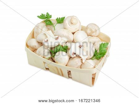 Fresh cultivated common button mushrooms and twigs of parsley in the wooden basket on a light background