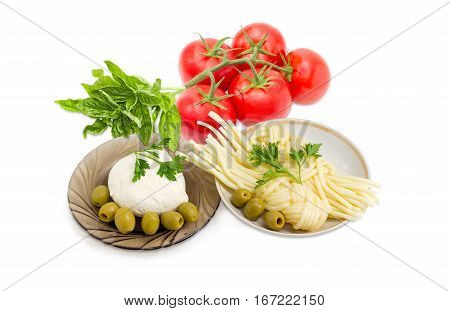 Ball of the fresh mozzarella cheese on the glass saucer mozzarella cheese twisted to form a plait on the other saucer green olives tomatoes basil and twigs of parsley on a light background
