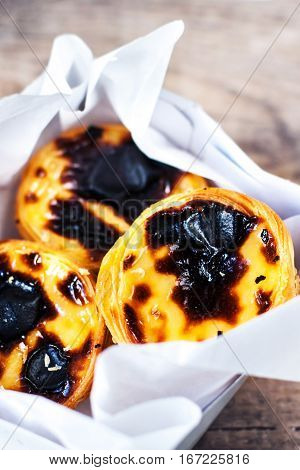 Pasteis de Nata - creamy egg tart with sweet curstard black crust and sugar powder on wooden background. Pasteis de Belem pastry