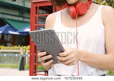 Portrait of young beautiful woman with red headphones and digital tablet. Outdoors. Urban concept.