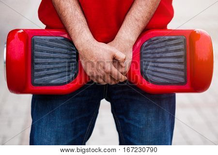 Man holding modern red electric mini segway or hover board scooter in hands. Trending new transportation technology that produces no air pollution to the atmosphere. African male model close up on device