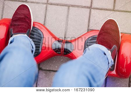 Close up on feet of a gir in marsala shoes riding on a modern red electric mini segway or hover board scooter. Trending new transportation technology that is so much fun and easy to ride and produces no air pollution to the atmosphere.