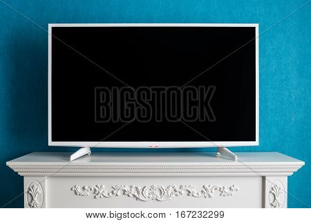 The white modern TV with the empty black screen. The TV costs on a curbstone with patterns on a background a wall with wall-paper of color of a sea wave