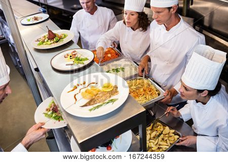 Chefs handing dinner plates through order station in the commercial kitchen