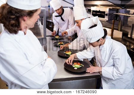 Head chef overlooking other chef decorating dish in the kitchen