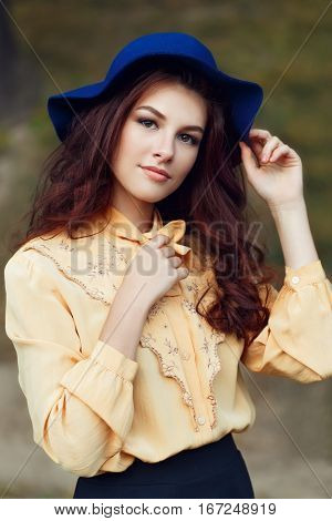 Outdoor closeup fashion portrait of sensual young stylish lady wearing trendy hat and blouse with bow. Fashion woman with curly hair and floppy hat. Young beautiful brunette girl with brown eyes