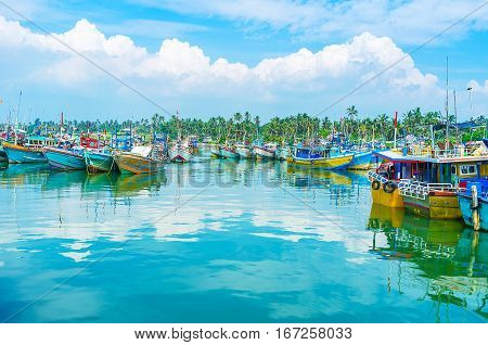 The bright azure seascape with numerous moored boats surrounded by jungles Mirissa fisheries harbor Sri Lanka.