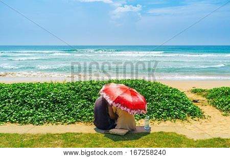 The young couple embracing under umbrella at the Beach Road in Matara Sri Lanka.