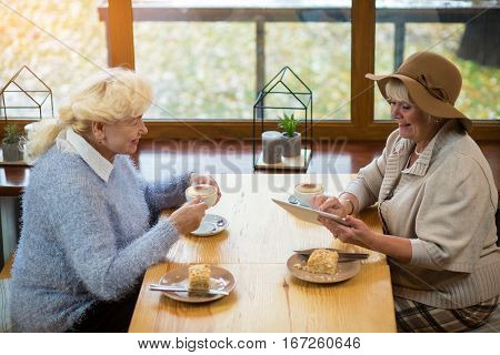 Senior women with a tablet. Coffee and cake on table. In step with the times.