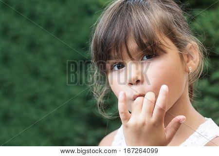 Portrait of brunette little girl licking her fingers outdoors. Girl is looking at the camera.