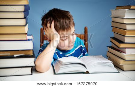 seven years old child reading a book at home. Boy studing at table on blue background