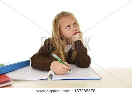sweet little schoolgirl in school uniform sitting at studying desk doing homework looking thoughtful and absent mind in child education concept isolated on white background