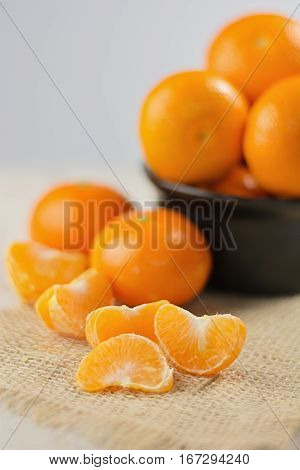 Group of tangerines in a small black bowl and peeled mandarin in the foreground.