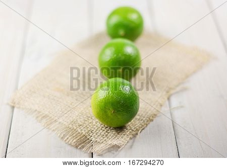 Three lime on the piece of cloth from a sacking on a wooden table.