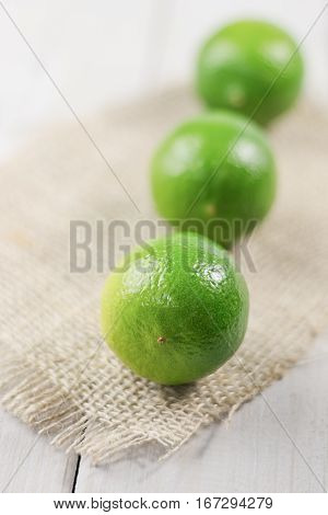 Three lime on the piece of cloth from a sacking on a wooden table.