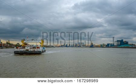 Woolwich ferry crossing the Thames on a stormy day at sunset.  The shot shows the Thames Barrier and the skyline of London beyond.