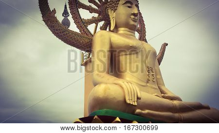 Close up low angle view of golden statue of sitting big Buddha with Samsara Wheel in Thailand