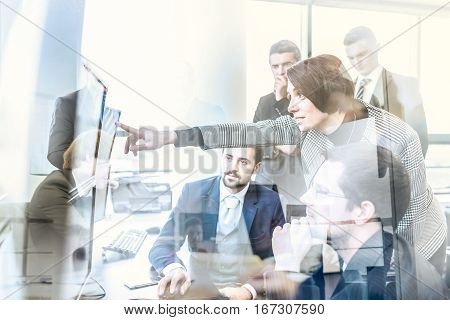 Business team looking at data on multiple computer screens in corporate office. Businesswoman pointing on screen. Business people trading online. Business, entrepreneurship and team work concept.