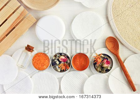 Cosmetic jars with facial scrub, cleansing gel, dried holistic herbs, wooden table top view. Healthy body care with natural ingredients.
