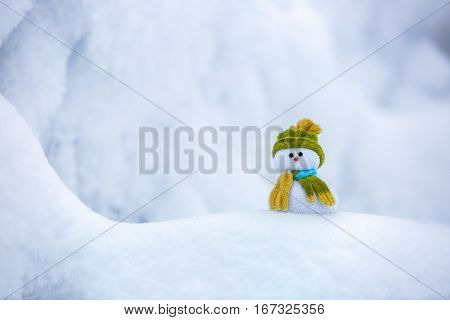 Nice dreaming snowman in green hat is standing on interesting textured snow near to the hill on cold winter day.