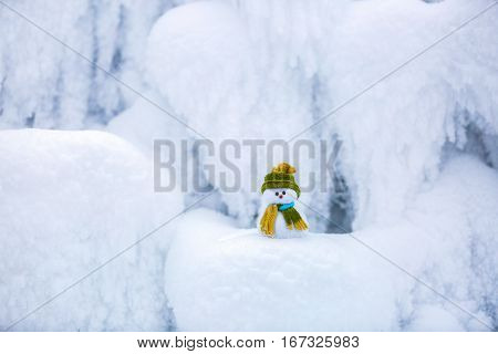 Snowman the Santa's assistant is standing in green hat wrapped with the scarf on nice textured snow on frosty winter morning.