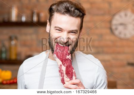 Handsome man biting raw meat on the kitchen