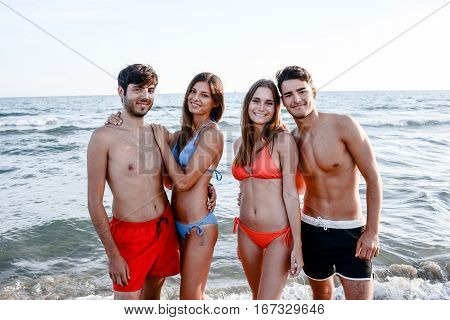 four happy friends young people man and woman having fun at ocean beach jumping together in the sea