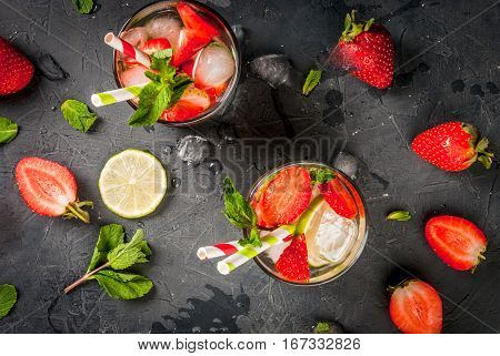 Summer refreshing mojito cocktail with strawberry mint and lime on a dark gray stone (concrete) table with shaker for whipping drinks top view