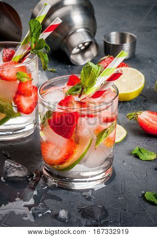 Summer refreshing mojito cocktail with strawberry mint and lime on a dark gray stone (concrete) table with shaker for whipping drinks