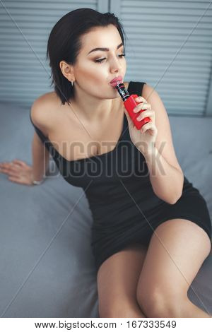 Woman holds an electro cigarette in a mouth and does steam inhaling.