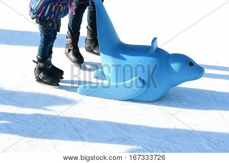 Family fun on outdoor ice rink, kid learning to skate with plastic seal as training aids