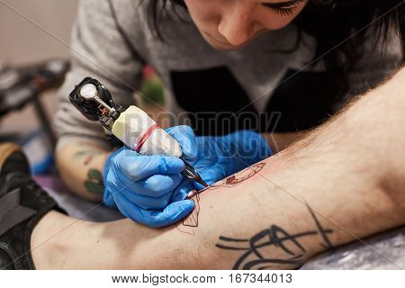 Tattoo artist is making tattoo. The process of creating a tattoo on the man's leg, closeup view. Machine for tattoos during work closeup