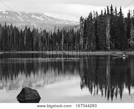 A man in a canoe at sunset with trees and the Middle Sister of Oregon's Cascade Mountains reflecting in Scott Lake on a summer day.