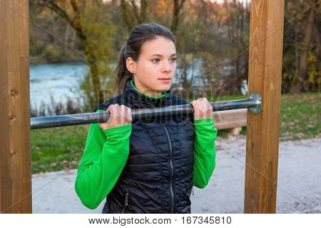 Attractive brunette doing pullups in park. Outdoor fitness.
