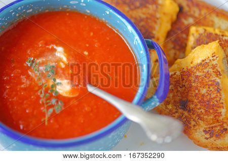 Tomato soup in an enamelware bowl with a grilled cheese sandwich cut in triangles