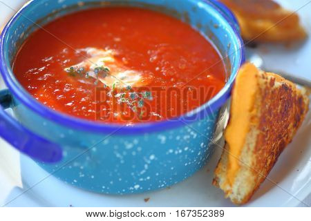 Tomato soup with fresh thyme in an enamelware bowl with a grilled cheese sandwich cut in triangles