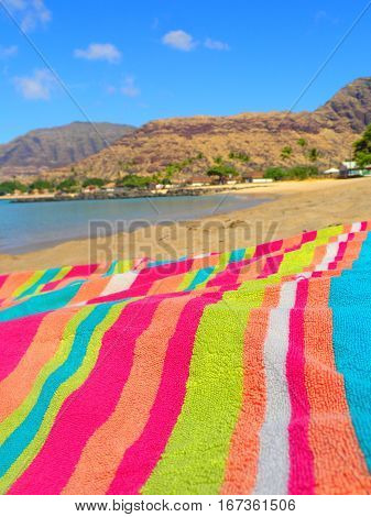 A brightly colored striped beach towel laying out on a beach at Pokai Bay Beach Park in Hawaii.