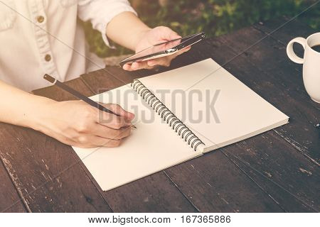 Close Up Hand Woman Writing Notebook And Holding Phone On Wood Table Backhround With Vintage Toned.