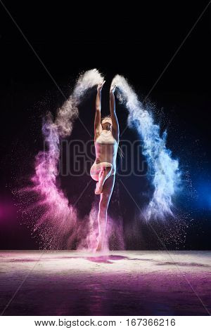 Slender girl jumping and streching her body emotionally in cloud of blue and pink dust studio shot