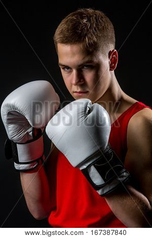 Young handsome boxer sportsman in red boxer suit and white gloves standing on black backgound. Copy space.