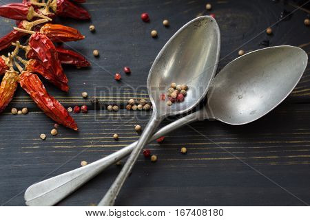Two old tin spoons with red hot chili cayenne peppers dried variety - spicy ingredient on wooden table