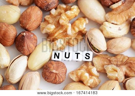 Raw mixed nuts and the word "nuts" spelled by tiled letter beads spread on a white table