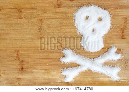 Deadly sugar addiction suggested by spilled white sugar crystals forming a skull on a wooden table